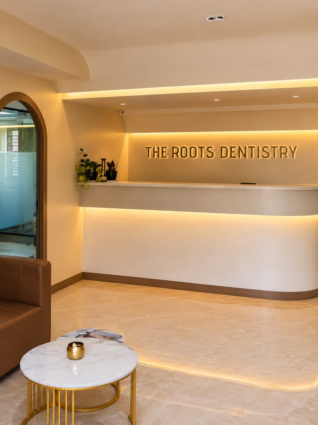 The reception at The Roots Dentistry, showing the room’s arched doorway, marble table and backlit brass signage